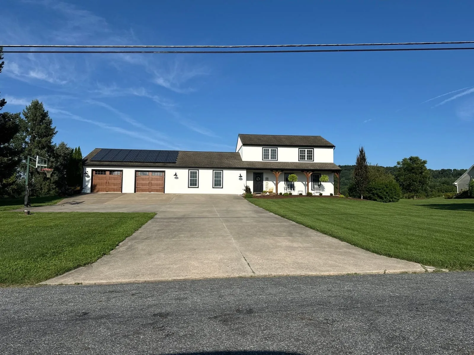 A white board and batten farmhouse with an attached garage, seen from the road on a clear day