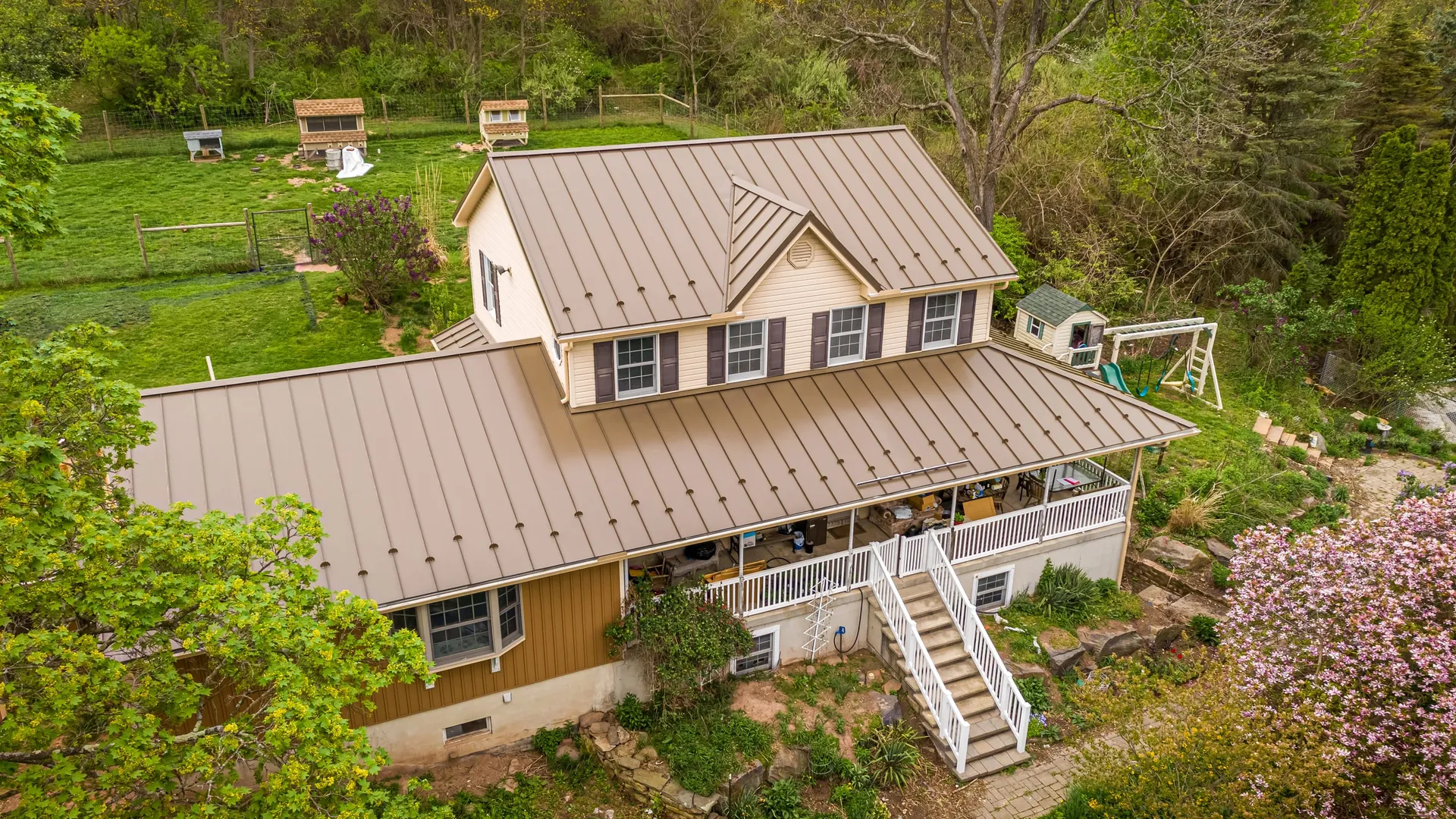 Aerial view of a tan standing-seam metal roof Esh Builders installed on a two-story Central PA home with a covered porch.