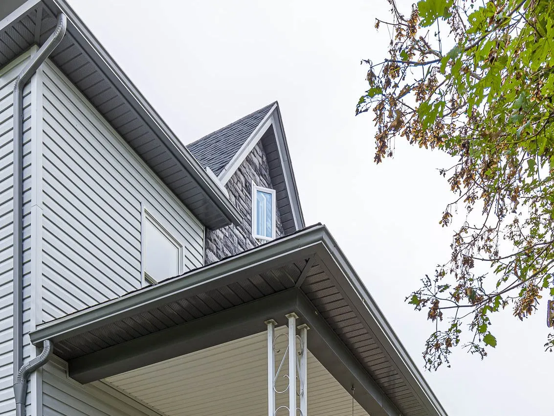 White seamless gutter and downspout on the upper story of a two-story home, with a color-matched gutter along the porch roof below